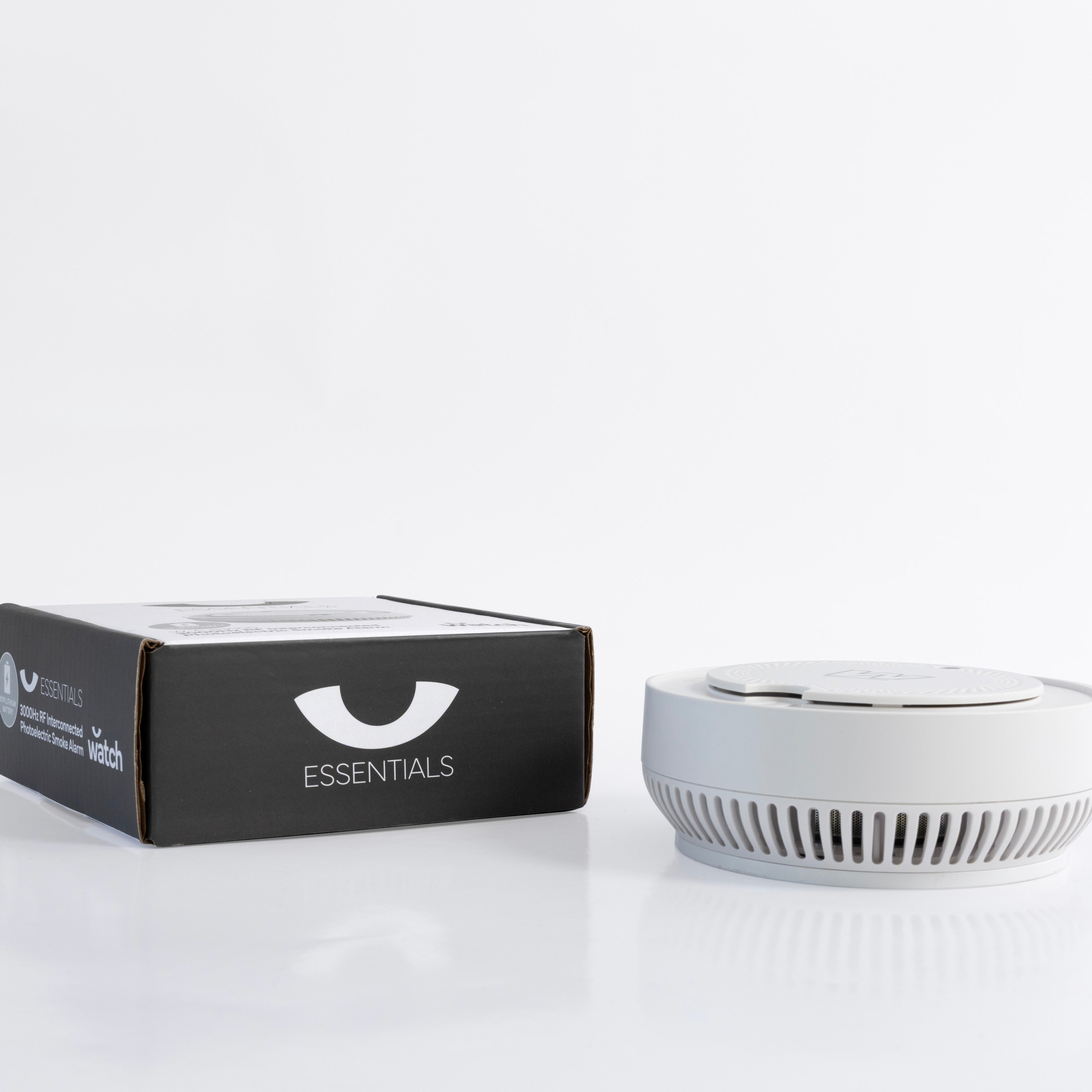 White smoke detector next to a black box labeled 'Essentials' on a white background